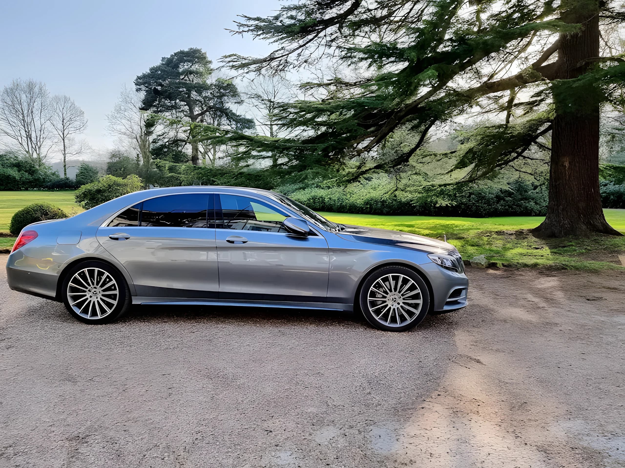 Silver Mercedes S-Class executive saloon on a gravel drive beside parkland